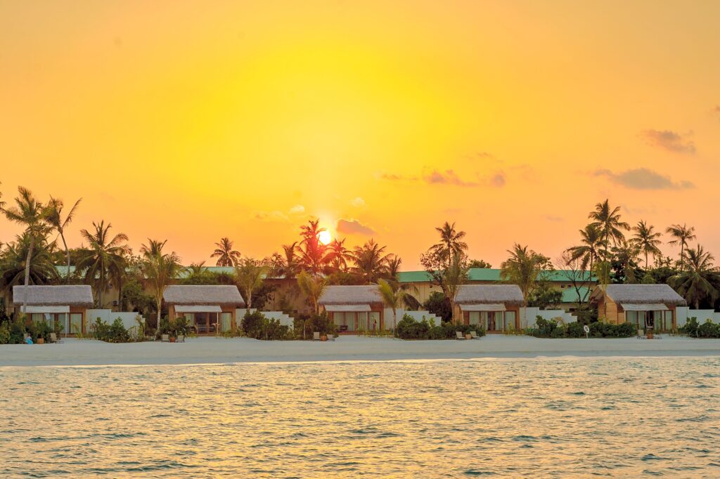 Breathtaking sunset over a tropical Maldives beach resort with palm trees and ocean view.